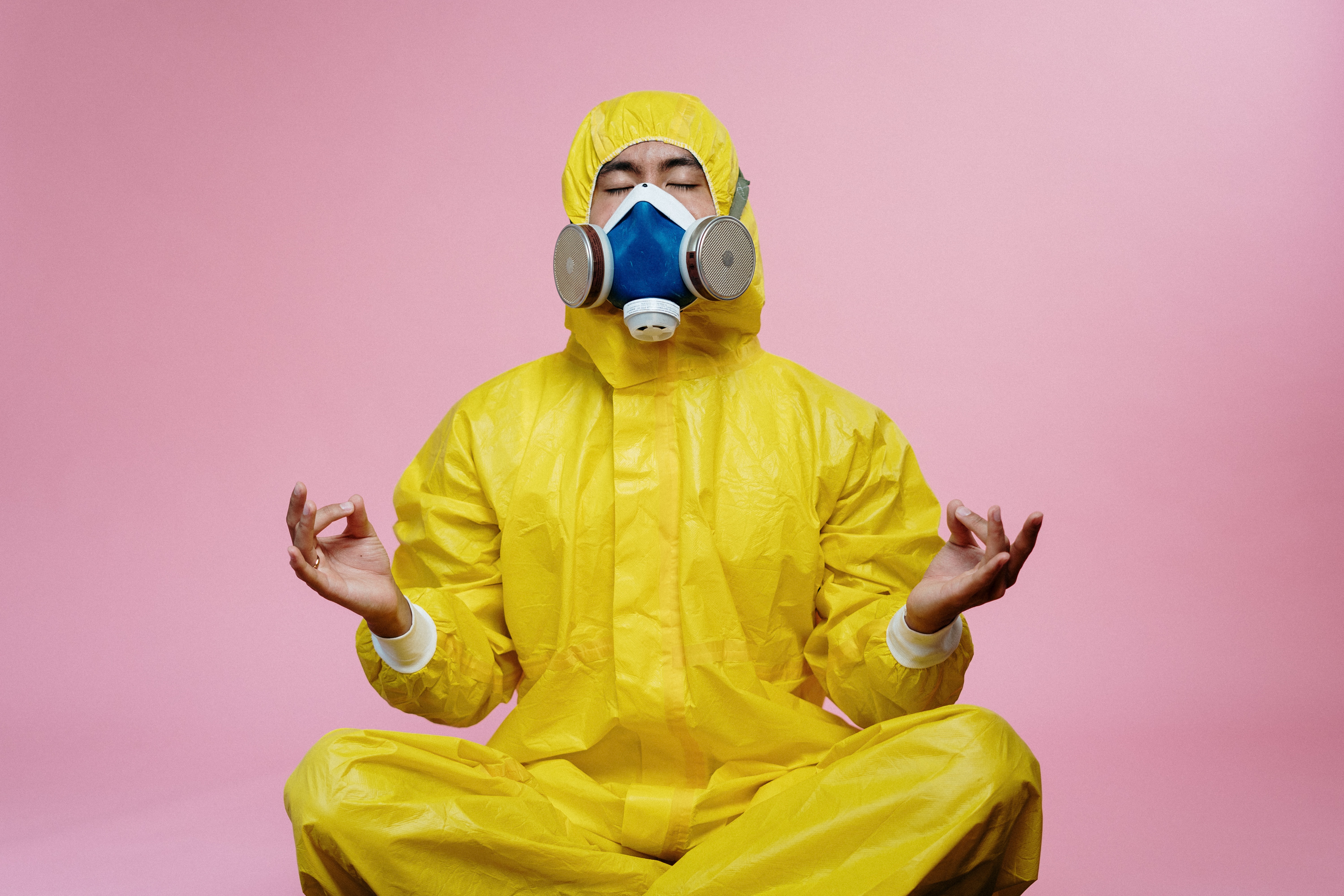 A person in  a yellow hazmat suit in a meditating pose. 