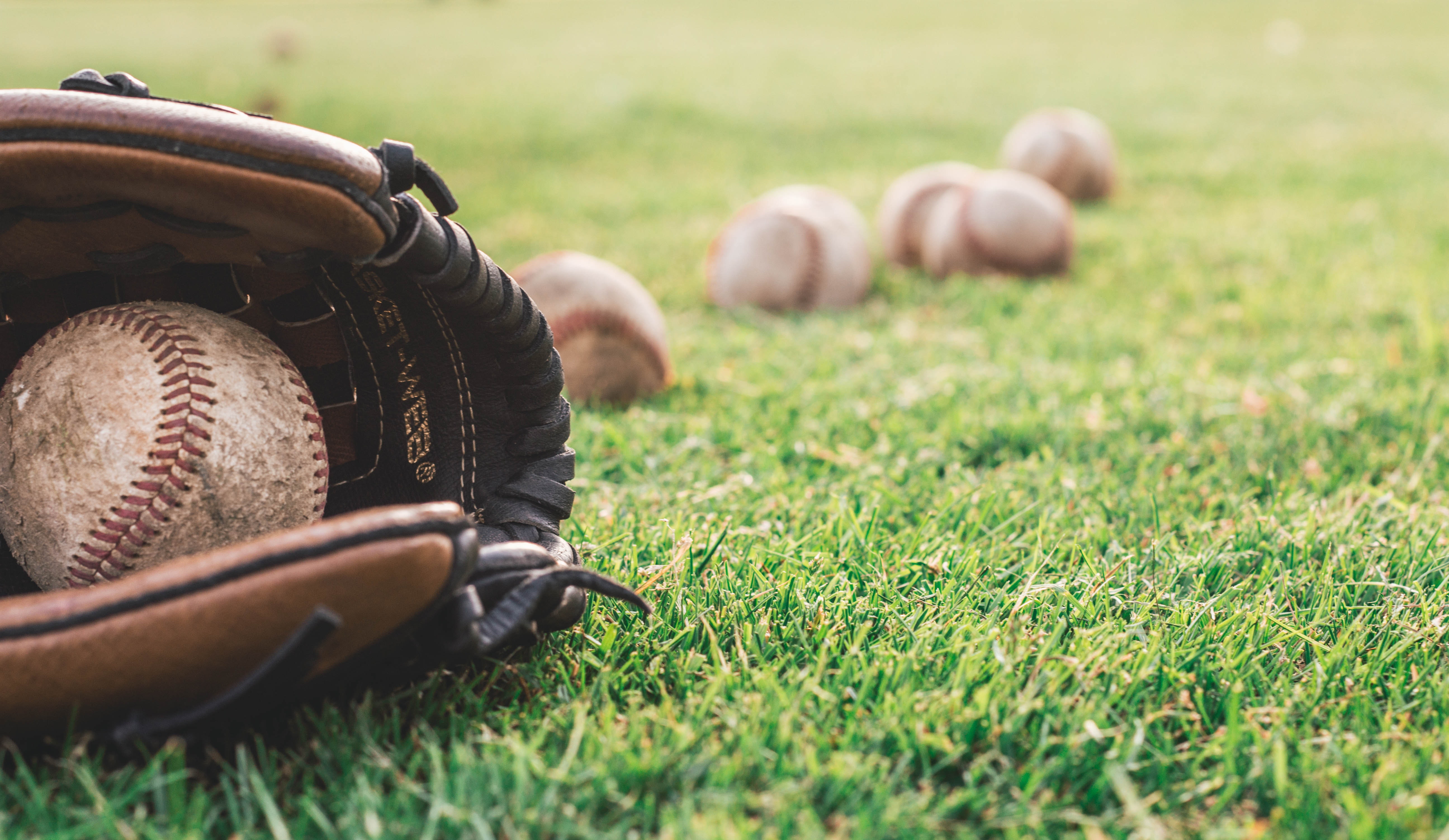 Baseball glove on some grass surrounded by more baseballs